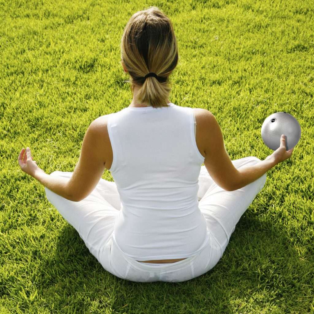 A woman sitting cross-legged on the grass holding a silver ChiBall